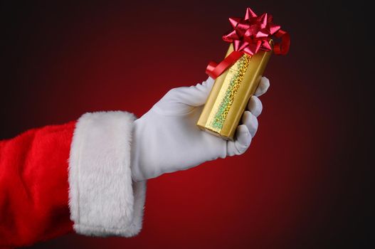 Santa Claus hand holding a wrapped Christmas present over a light to dark red background.