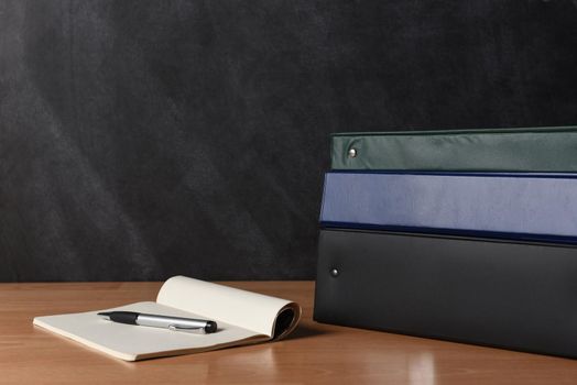 Teachers desk with note pad and pen and a stack of different colored binders.