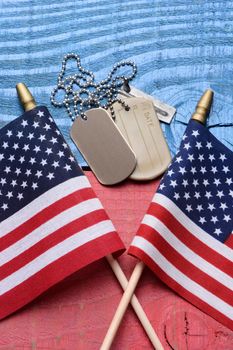 Overhead shot of a set of dog tags and two American flags on a red white blue patriotic table. Vertical format. Useful for 4th of July, Memorial Day and Veterans Day projects.