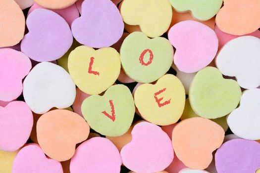 Macro shot of pastel candy hearts for Valentine's Day. Four of the candies have the word LOVE spelled out in individual letters. 