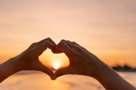 Woman hand do heart shape on sunset sky and bokeh background.