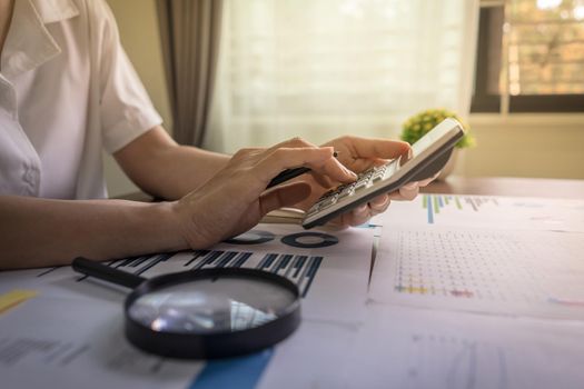 Auditors are using calculators to check financial audits, company earnings data, income and loss statistics on the table with a magnifying glass. Accounting and Business Concept.