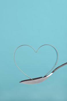 Heart shaped cookie cutter balanced on a spoon against a teal background. love, baking, 