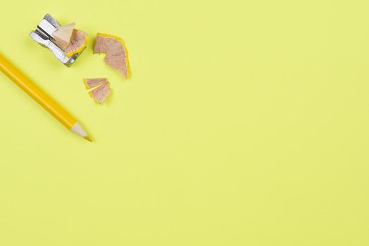 Yellow Pencil and Sharpener on a yellow background. The pencil with shavings is shot from a high angle with copy space. Back to School theme.