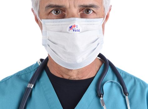 Closeup of a doctor with an I Voted sticker on the COVID-19 protective mask he wore to vote. The man is wearing surgical scrubs with a stethoscope.