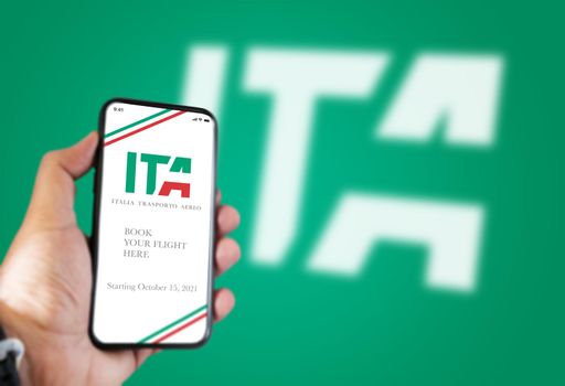 Rome, Italy, july 2021: A hand holding a phone with the ITA app on the screen and the ITA logo Blurred on a green background.ITA is the new Italian flag carrier starting from 15 October 2021