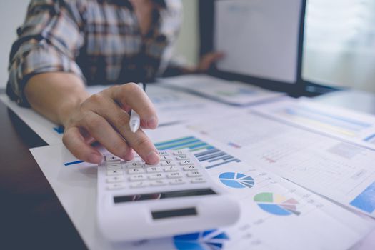 Businessman or Accountant is using a calculator to calculate financial information from a folder on the table with graph statistics document, company earnings data, income and loss statistics