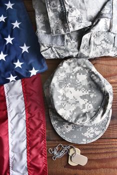 Top view of military fatigues, dog tags and American Flag on a wood background. Military service concept for Memorial Day, Veterans Day and Patriotic events.