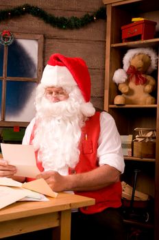 Santa Claus Sitting in His Workshop reading a letter. Vertical Composition.