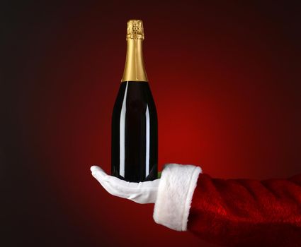 Closeup of Santa Claus holding a bottle of Champagne in the palm of his outstretched hand. Hand and arm only over a light to dark red spot background.