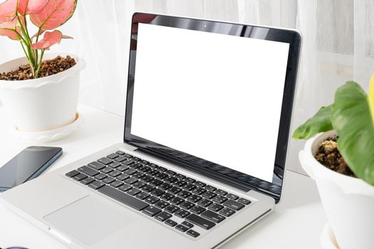 Modern workspace, mock up laptop computer blank white screen, eyeglasses and smartphone white table have potted plants on the desk, Notebook and mobile phone on desktop home office