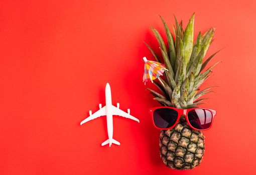 Celebrate Summer Pineapple Day Concept, Top view flat lay of funny fresh pineapple wear red sunglasses with model plane, isolated on red background, Holiday summertime in tropical