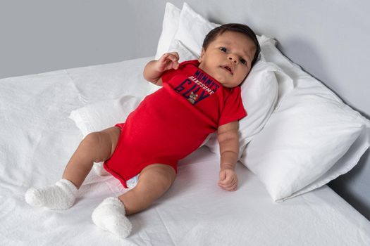 Infant lying on his back with his head on some pillows, wearing red clothes