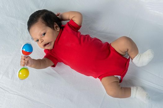 Infant lying on his back wearing red clothes holding a toy in his hand