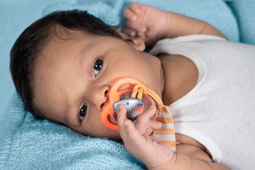 Infant lying on his back facing the camera, with a tete in his mouth