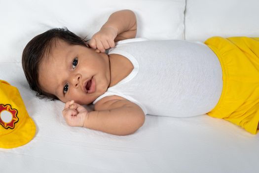 Infant lying on his back wearing a white t-shirt and yellow shorts