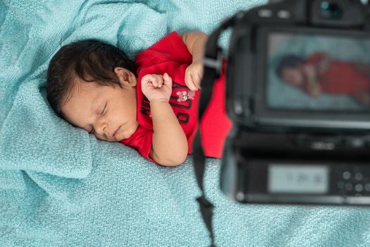 Infant asleep lying on his stomach, dressed in red clothes and a camera with his image on its screen