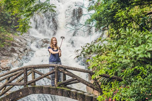Excited female tourist making self portrait in front of the waterfall. Woman having a great vacation in Vietnam.