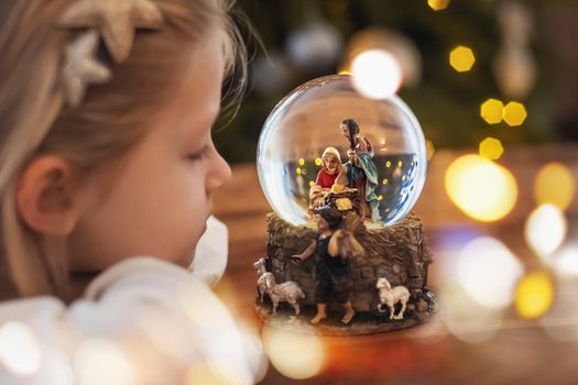 Girl looking at a glass ball with a scene of the nativity of Jesus Christ in a glass ball