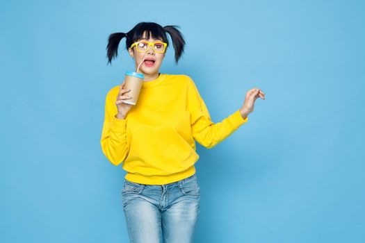cheerful woman with pigtails in yellow sweater drink blue background. High quality photo