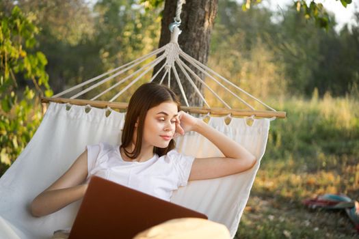 cheerful woman lies in a hammock with a laptop vacation internet travel. High quality photo