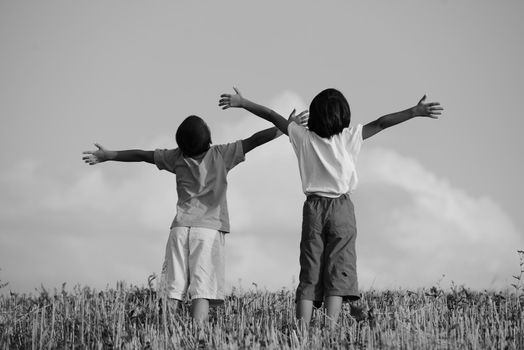 Two kids standing on meadow with arms up in air