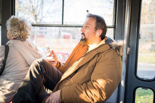 Man in public transport sitting with smartphone listening to the music