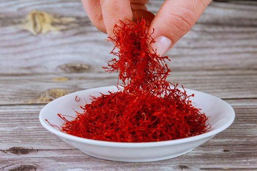 The girl puts the saffron in a white plate. Saffron spice on a wooden background.