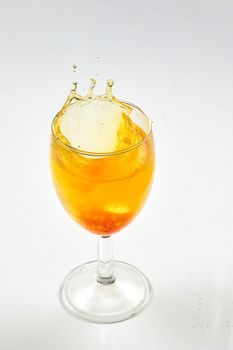 A dice falling into a glass of orange liquid caused a splash. Close up on white background