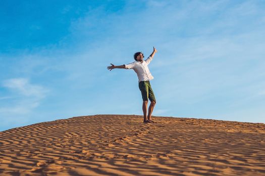 Beautiful young man jumping barefoot on sand in desert enjoying nature and the sun. Fun, joy and freedom.