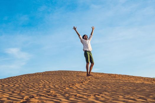 Beautiful young man jumping barefoot on sand in desert enjoying nature and the sun. Fun, joy and freedom.