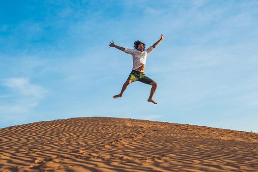 Beautiful young man jumping barefoot on sand in desert enjoying nature and the sun. Fun, joy and freedom.