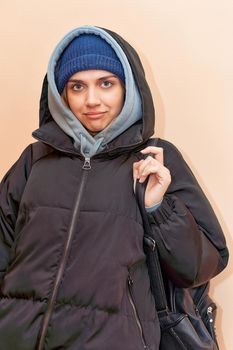 Facial portrait of a pretty girl in a hat and dark jacket with a hood looking at the camera