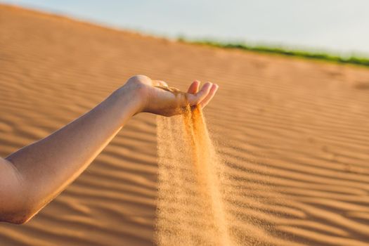 Sand slipping through the fingers of a woman's hand in the desert.