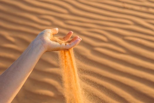 Sand slipping through the fingers of a woman's hand in the desert.