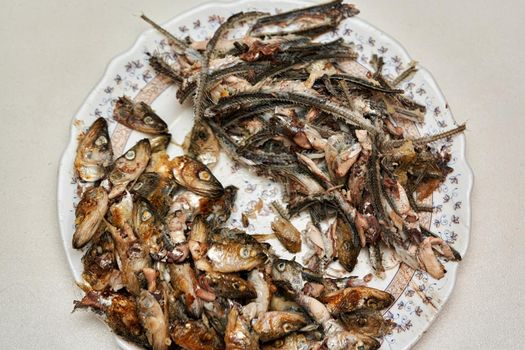 Fish heads and bones left after eating on a plate. Fried fish skillet on a light background. Fish skeletons