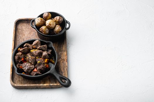 Beef meat stewed with potatoes, carrots and spices set, in cast iron frying pan, on white stone surface, with copy space for text