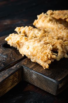 Crispy chicken tenders cuts on dark wooden background.