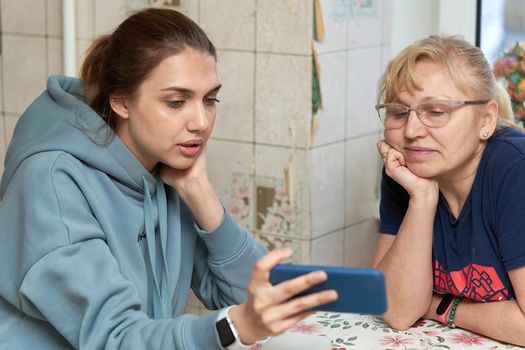 The girl shows her mother photos on the smartphone while sitting at the table. Family values