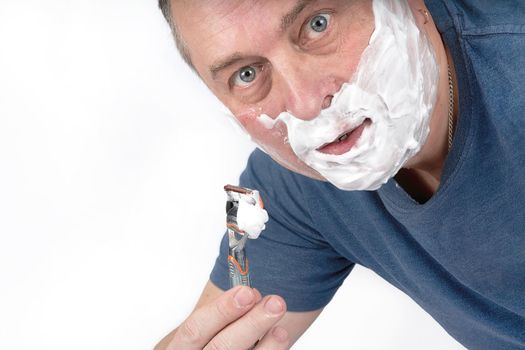 A man face in shaving foam shaves with a safety razor. Morning or evening exercise, personal hygiene