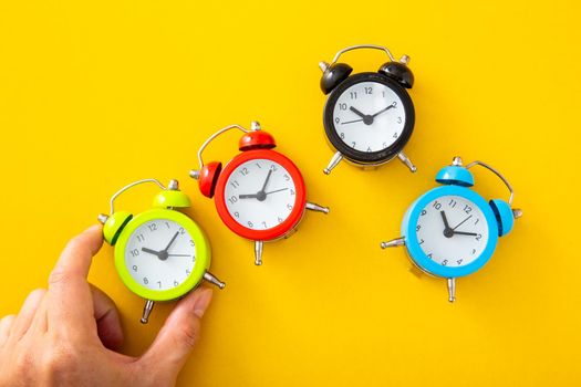 Hand choosing a green alarm clock on isolated yellow background.