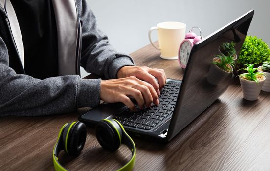 An Asian man uses a laptop at home while sitting at a wooden table. The concept of work from home.