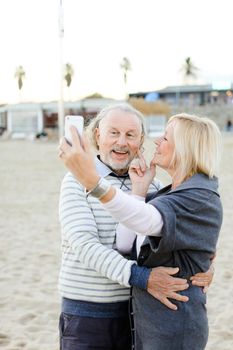 Elderly caucasian couple making selfie by smartphone on sand beach. Concept of pensioners and modern technology.