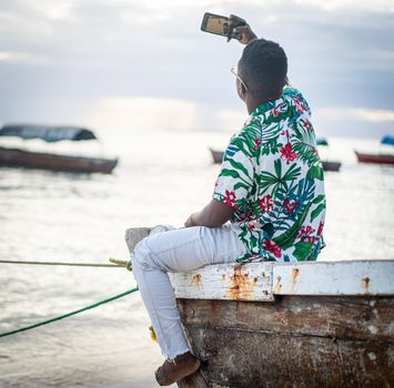 Young black man sitting on boat taking selfie alone