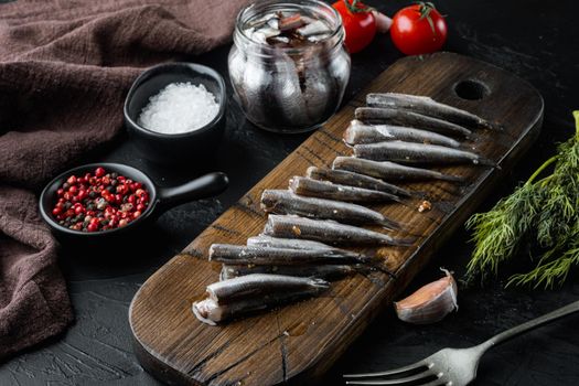 Salted anchovy fillets set, on wooden cutting board, on black background with herbs and ingredients