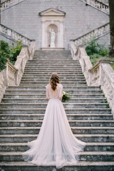 Bride stands on stone steps in the garden near the old building. High quality photo