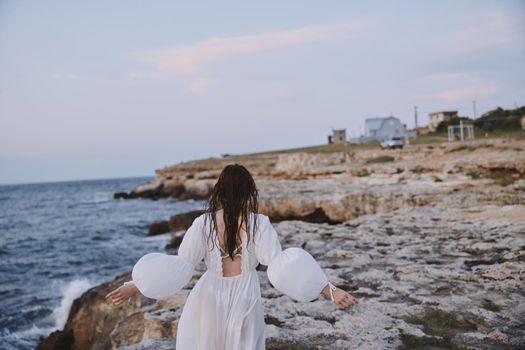 Woman in white dress walks on the beach stones back view. High quality photo