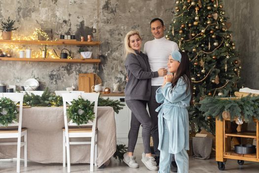 Christmas Family. Happiness. Portrait of dad, mom and daughter at home near the Christmas tree, all are smiling.