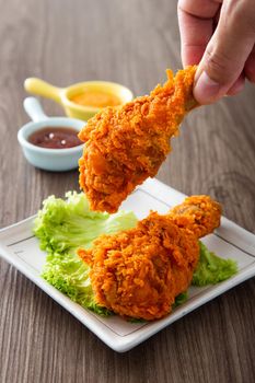 hand holding crispy and golden fried chickens with sauce on wooden table