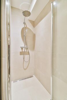 Shower faucet hanging on white tiled wall in light washroom in modern flat